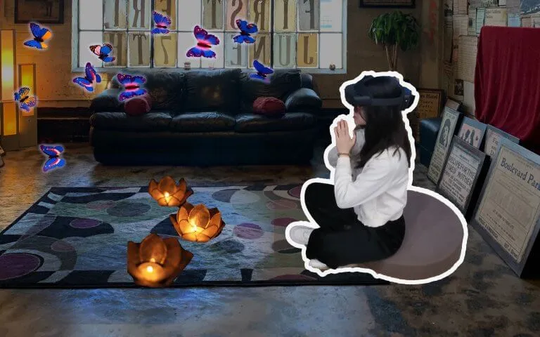 A person wearing a HoloLens sits on a cushion, with virtual butterflies and lotus lanterns around them