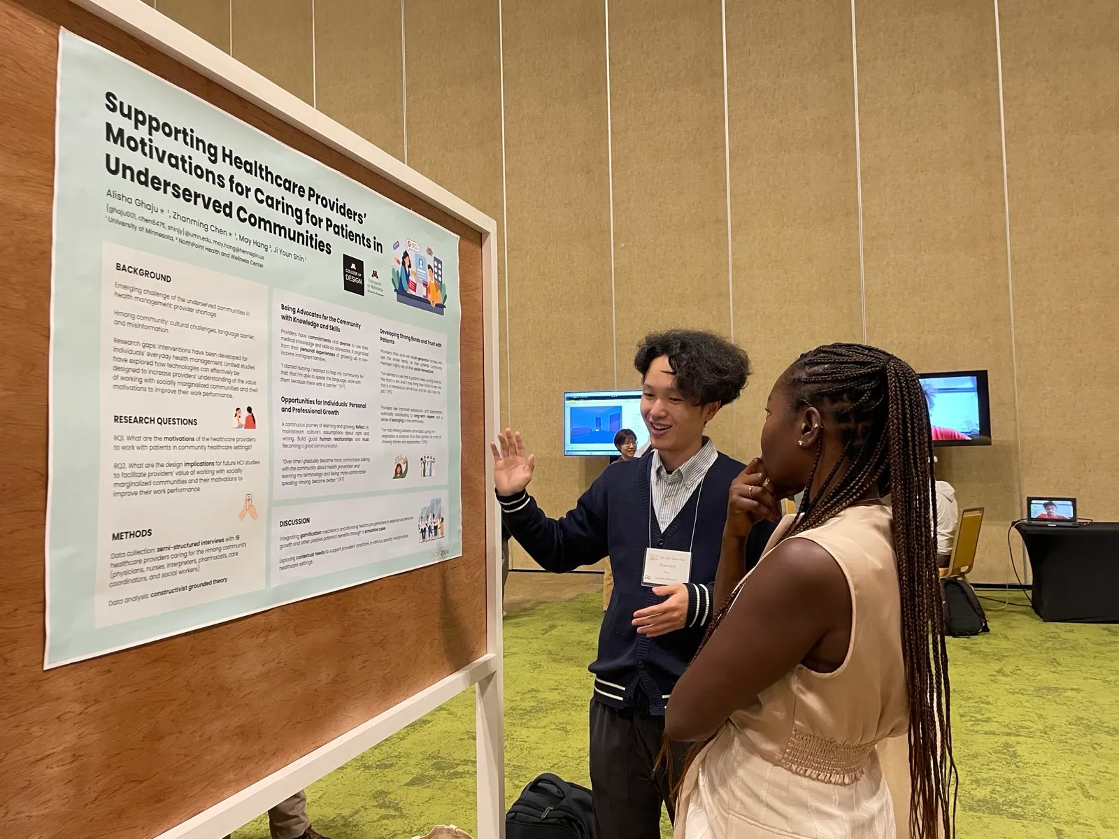 Zhanming Chen smiles and gestures toward the poster as an attendee listens.